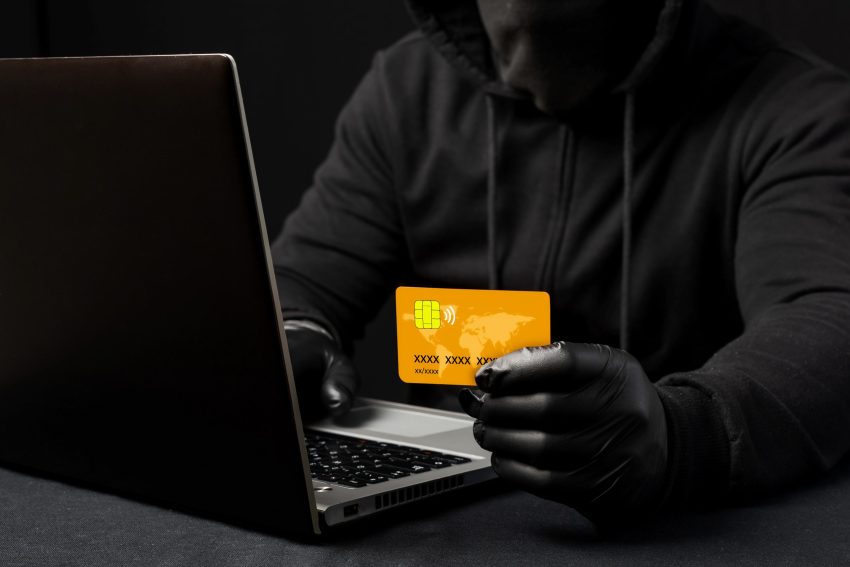 A hooded cybercriminal, holding a credit or debit card. Internet scams. Phishing alert. Violated access to personal data